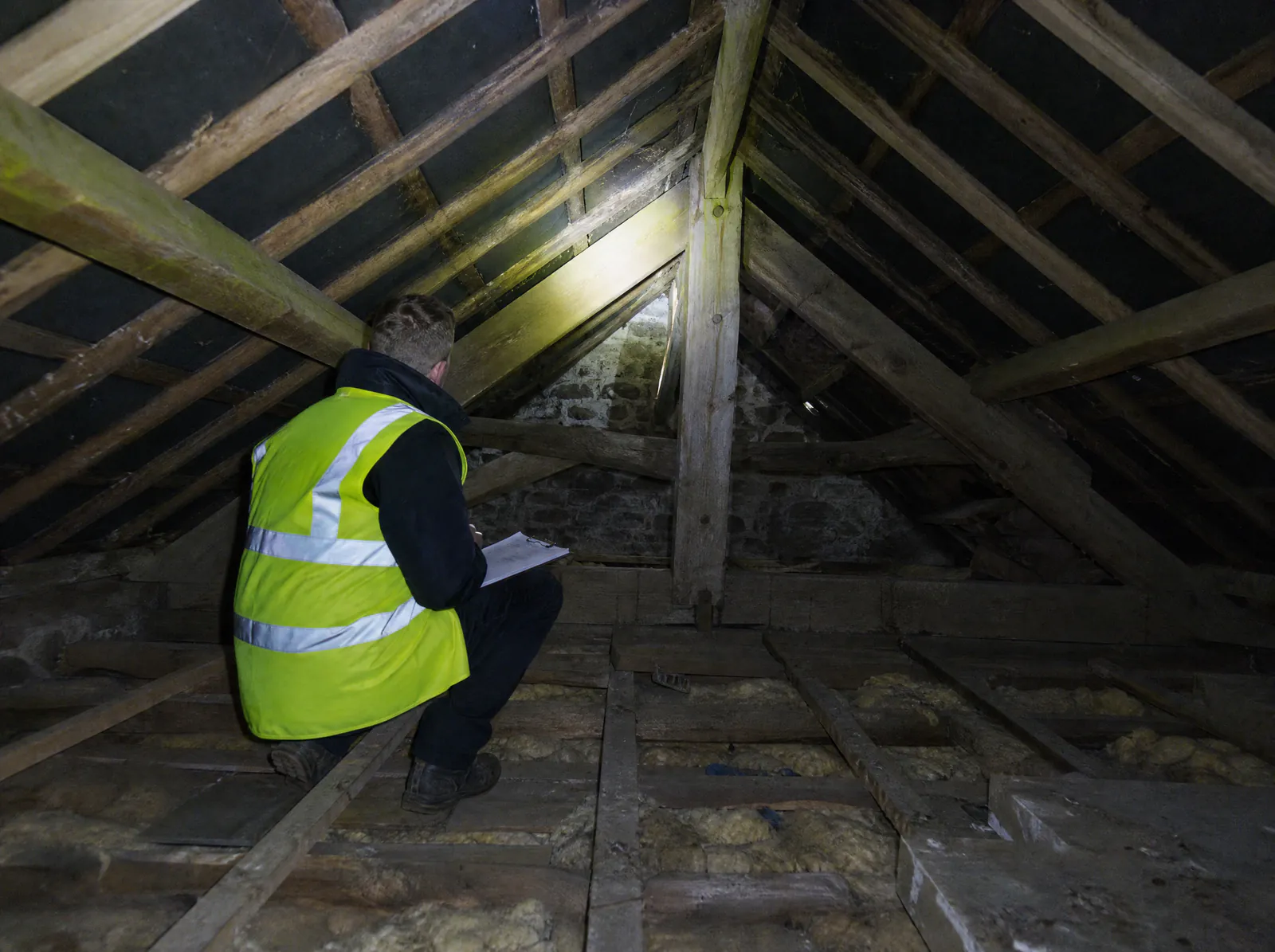 Engineer inspecting roof timbers by torchlight in an attic during a pre-purchase structural survey